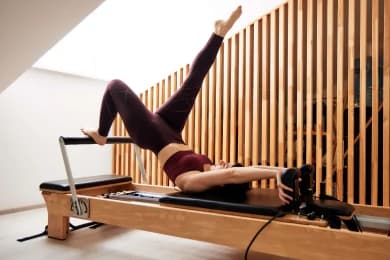 Na foto, uma mulher está em estúdio de pilates realizando uma atividade da modalidade, que também ajuda a alongar as pernas. #ParaTodosVerem